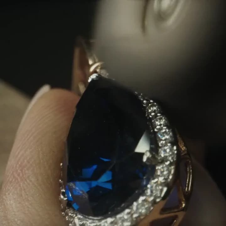 A royal blue Ceylon sapphire with a diamond halo, turned to the light in the atelier